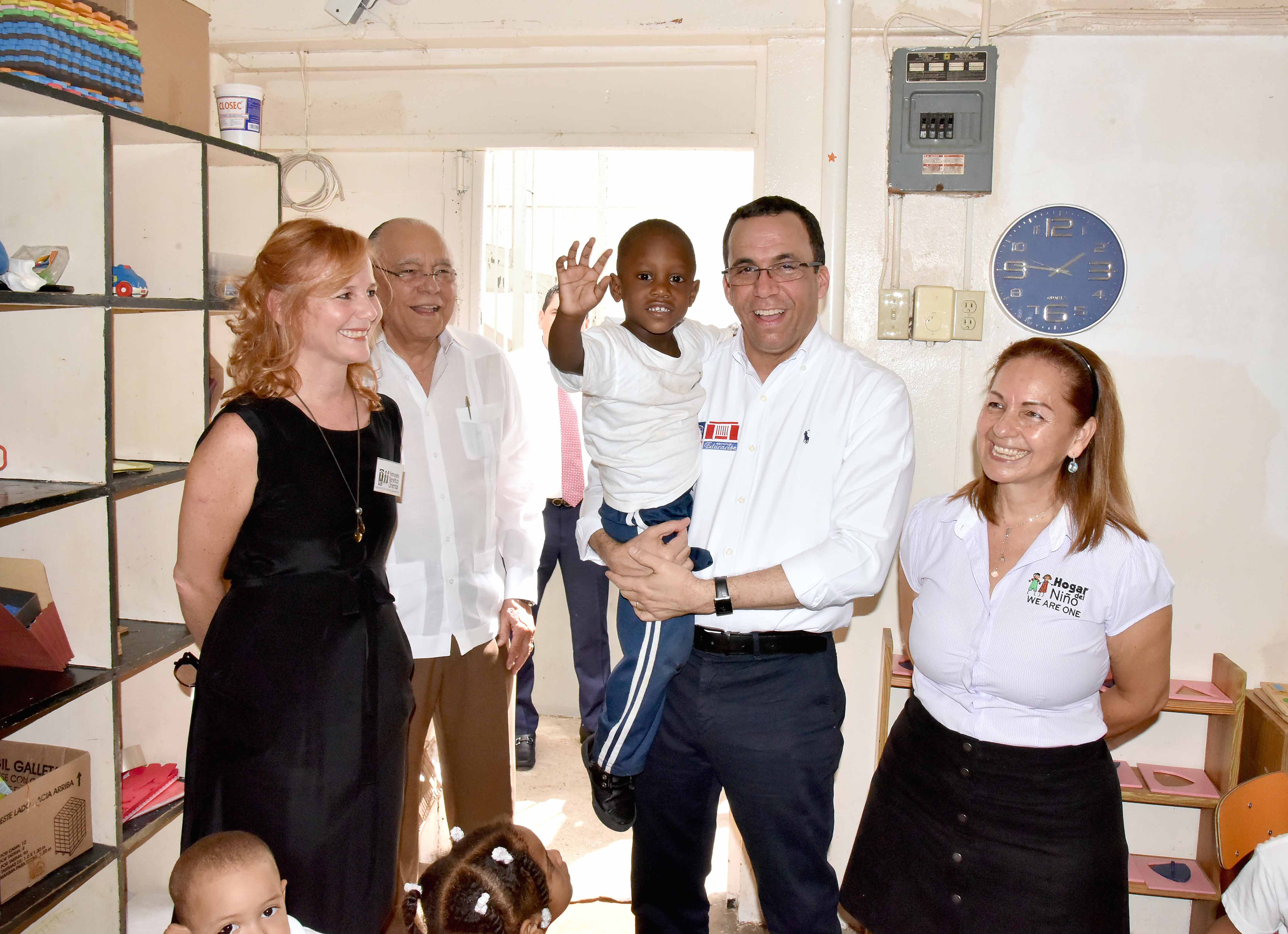  imagen Ministro Andrés Navarro soriendo mientras carga a niño rodeado por miembros del Patronato Benéfico Oriental. 
