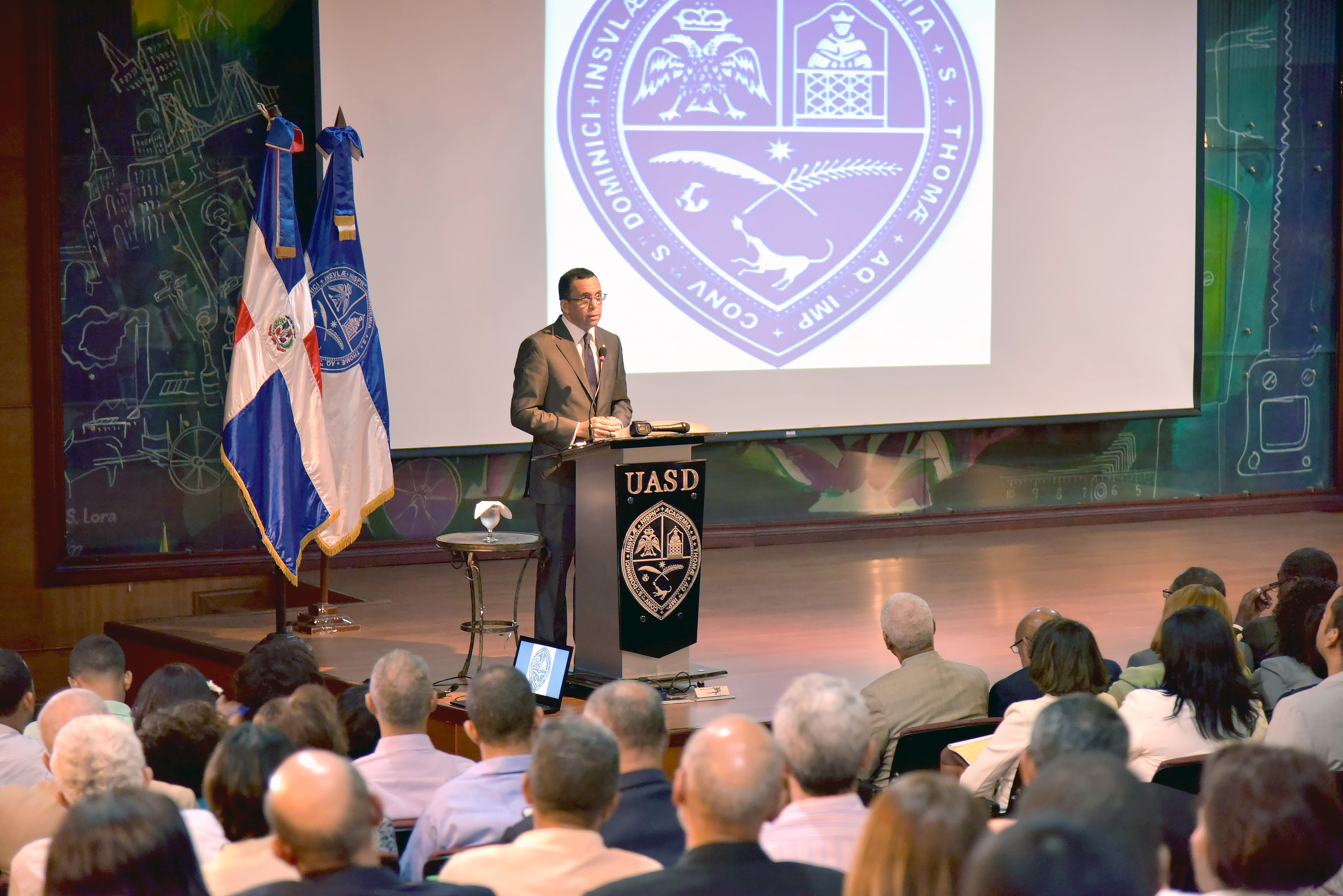  imagen Ministro Andrés Navarro de pie desde podium en auditorio en la UASD se dirige a cientos de personas  