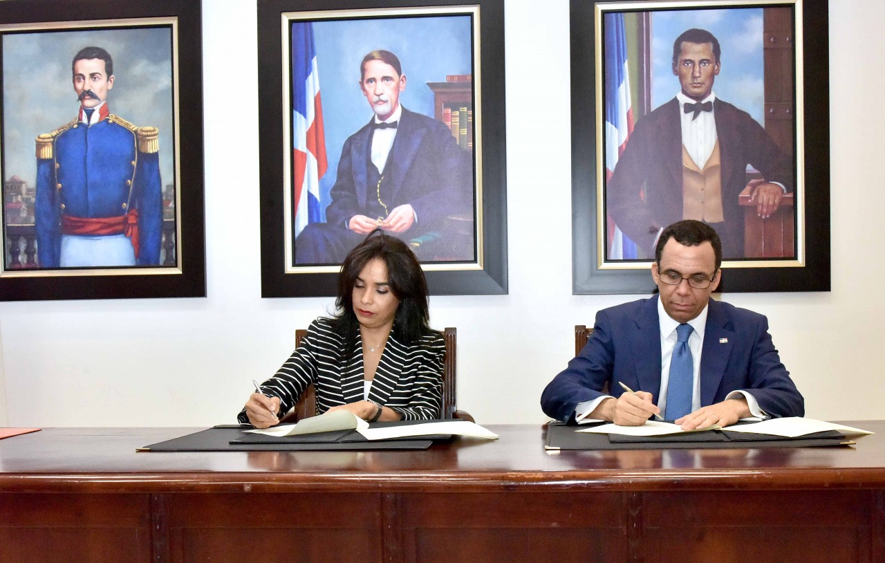  imagen Ministro Andrés Navarro y Directora de INTRANT, Claudia Franchesca De Los Santos sentados firmando acuerdo interinstitucional  