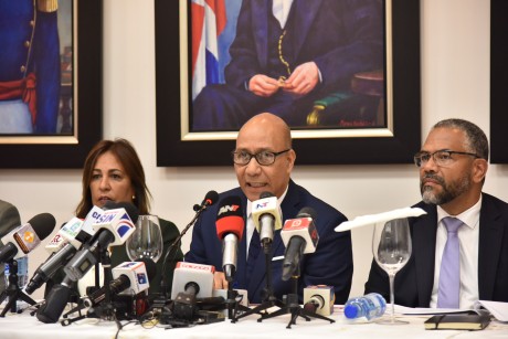  imagen Henry Santos junto a otras personalidades, sentados frente a la prensa durante rueda de prensa. 